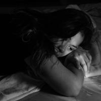 En ung trist kvinde ligger på maven i sin seng og kigger ned. 